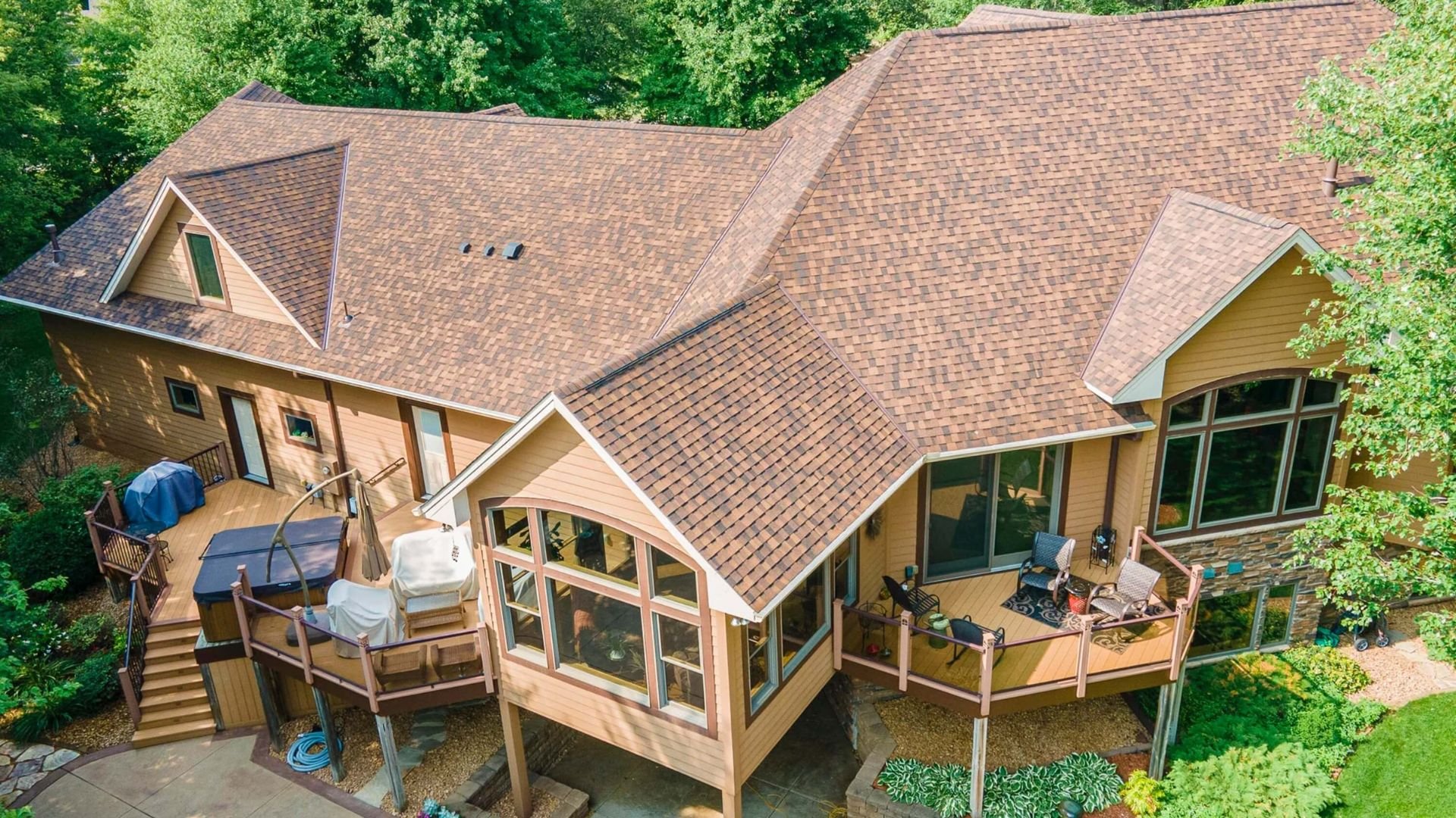 Large wooden house with multi-level deck surrounded by green trees