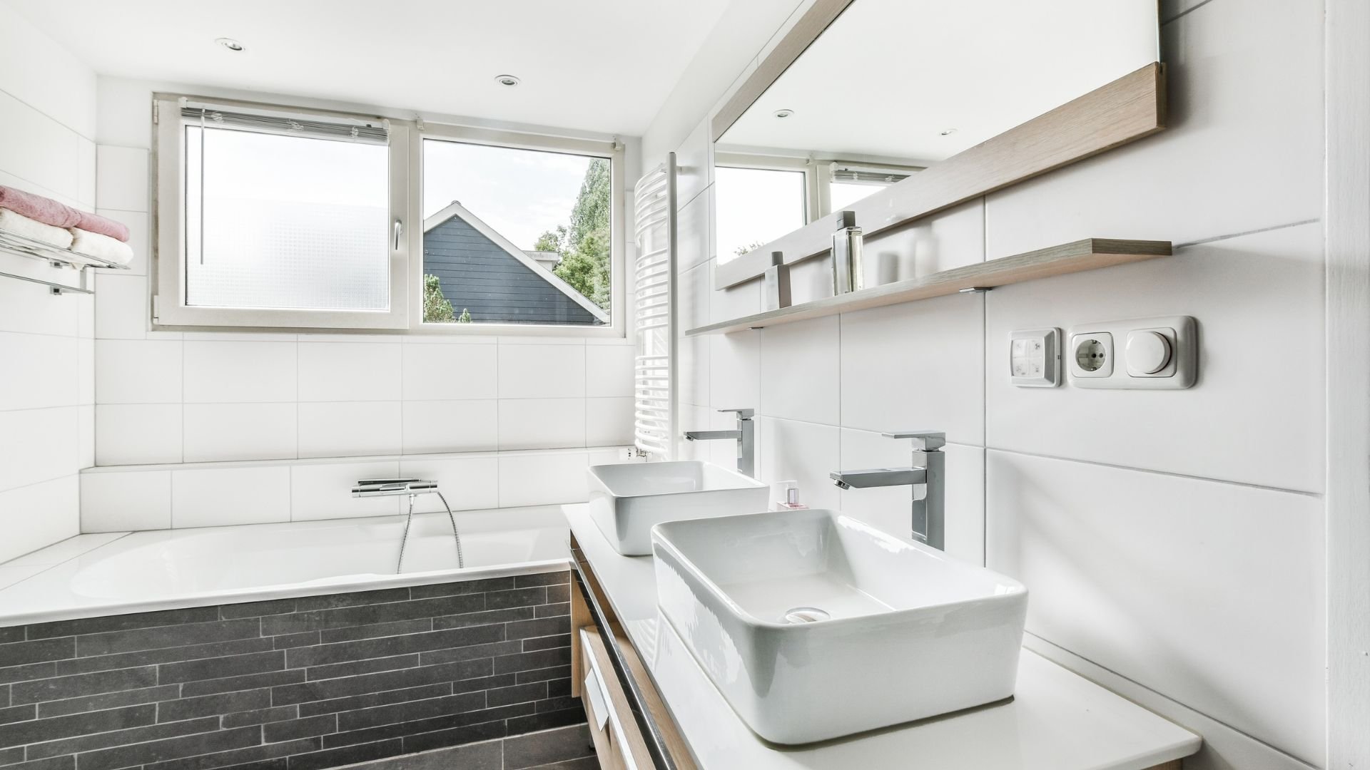 Modern white bathroom with bathtub, two sinks, and large windows